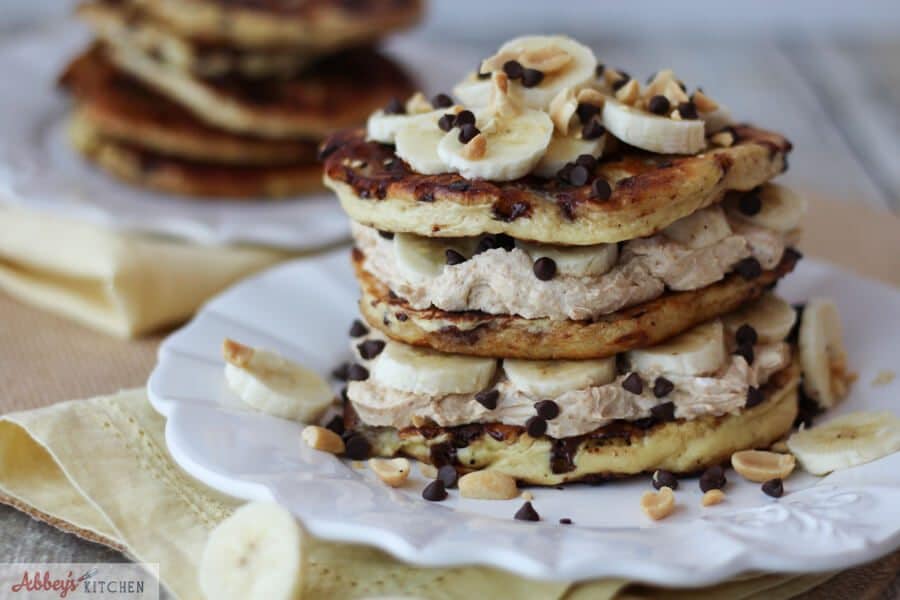 Peanut butter protein pancakes stack on a white plate topped with bananas and mini chocolate chips.