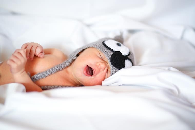 Baby lying in bed with a hat on. 