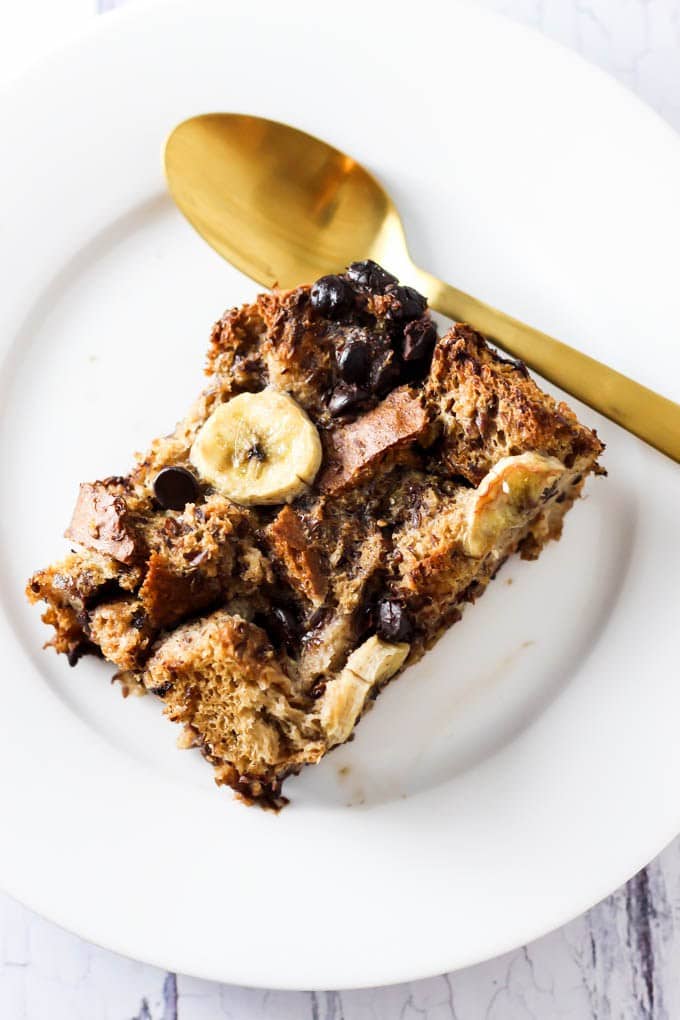 Banana chocolate chip french toast casserole on a white dish with a gold spoon. 