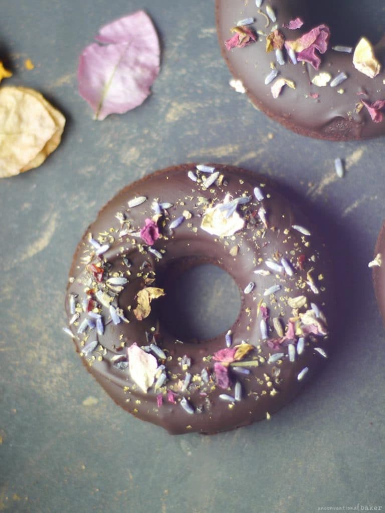 A close up of a raw chocolate donut with colourful sprinkles on top.