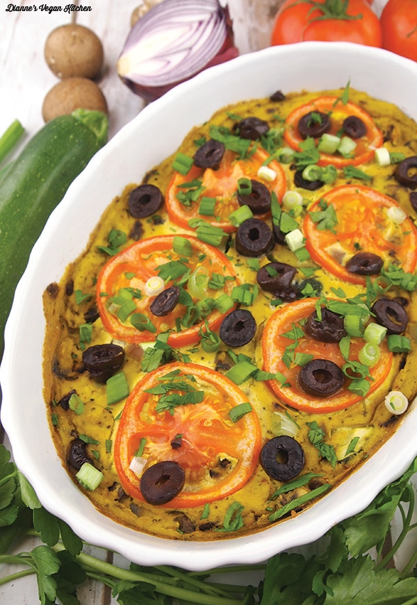 Tofu frittata with tomatoes, olives and green onions in a white serving dish. 