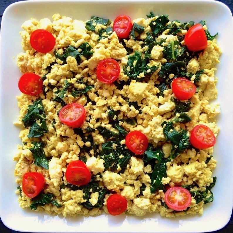 Tofu scramble with spinach and tomatoes in a white serving dish. 