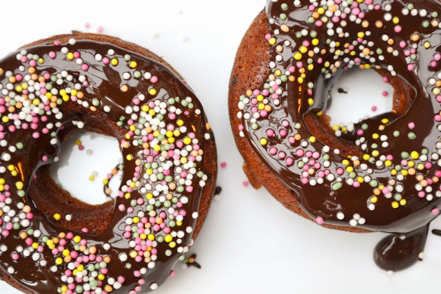 A close up of a triple chocolate donut with colourful sprinkles.