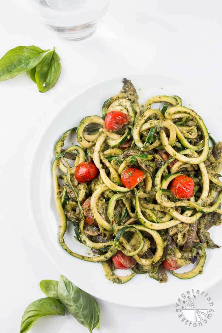 Pesto zucchini spaghetti with tomatoes on a white plate. 