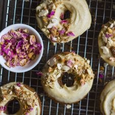 An overhead image of baked banana bread almond donuts with dried petals on top.