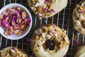 An overhead image of baked banana bread almond donuts with dried petals on top.