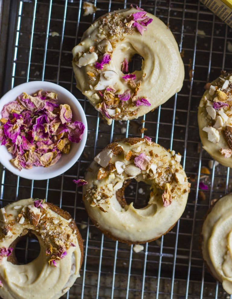 An overhead image of baked banana bread almond donuts with dried petals on top.