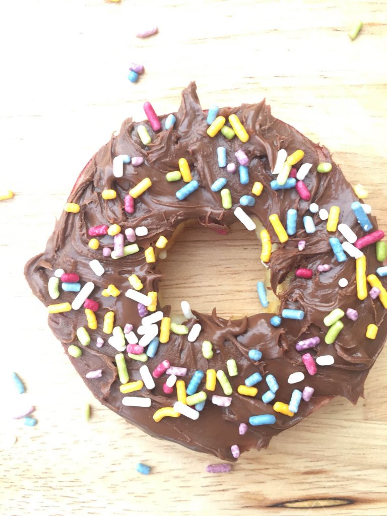 An overhead photo of an apple donut with chocolate frosting and rainbow sprinkles.