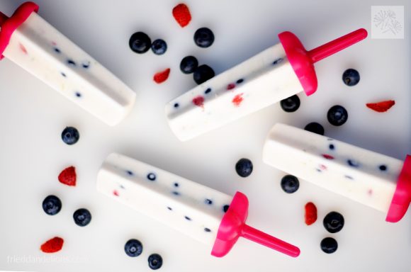 Four firecracker popsicles with fruit scattered around it.