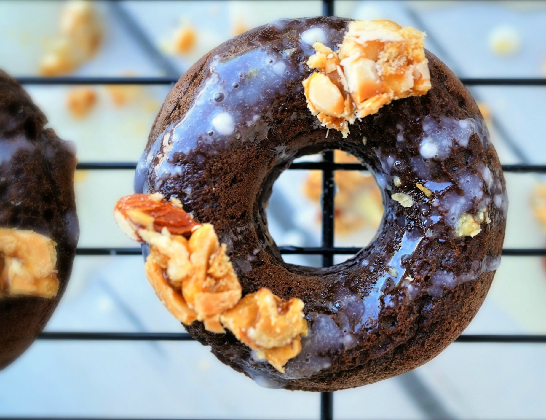 A close up of a chocolate peanut brittle baked donut on a cooling rack. 