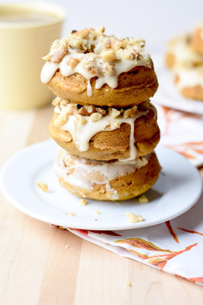 Three maple walnut pumpkin donuts stacked on a white plate.