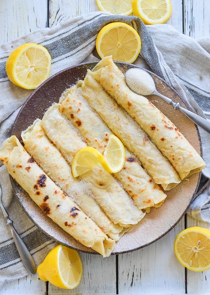 English pancakes on a brown plate topped with lemon slice garnish. 