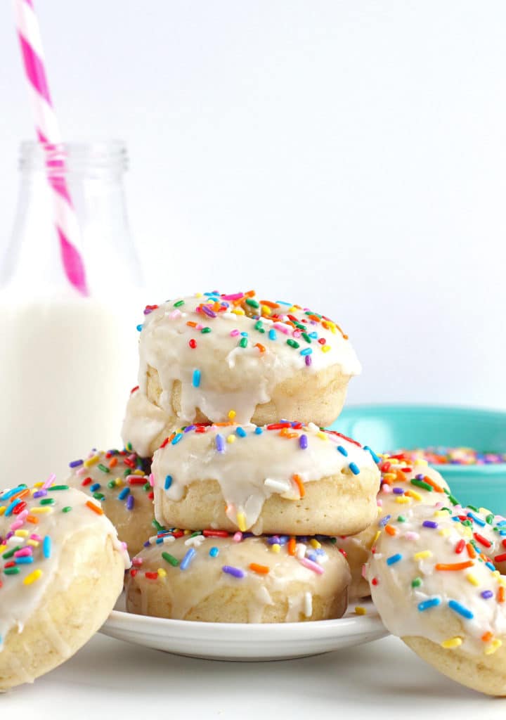 A stack of vanilla cake donuts with rainbow sprinkles on top.