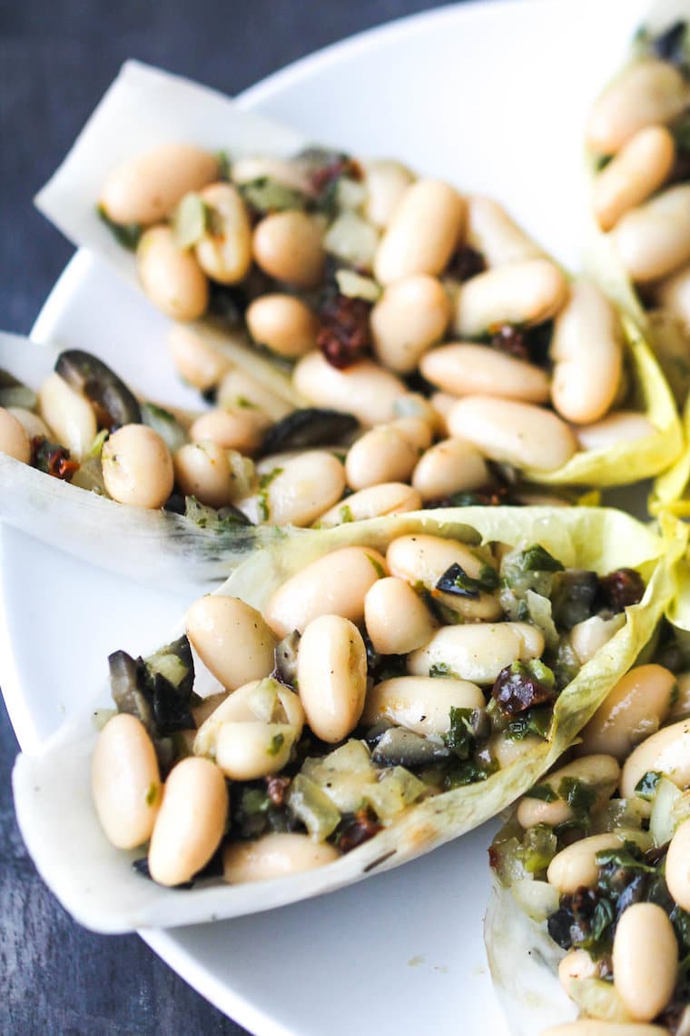 Close up image of vegan cannelini bean salad with basil and sundried tomatoes served inside lettuce cups presented on a large white serving dish