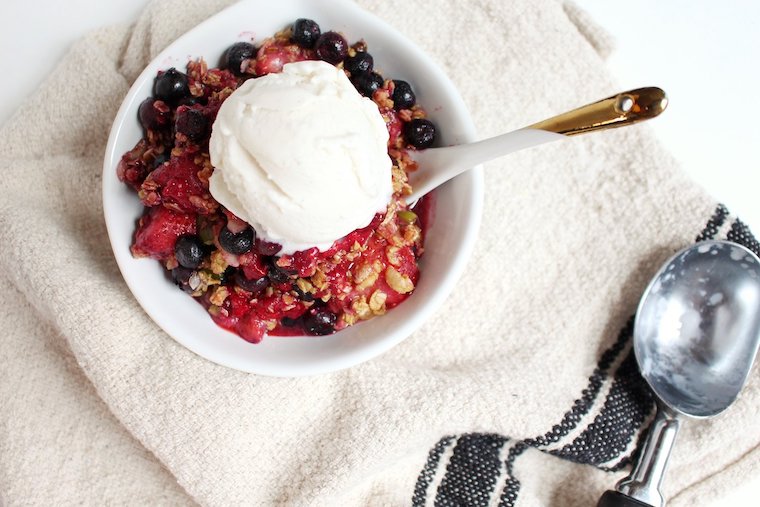 Birds eye view image of a plant-based berry crisp in a white bowl garnished with vanilla ice cream