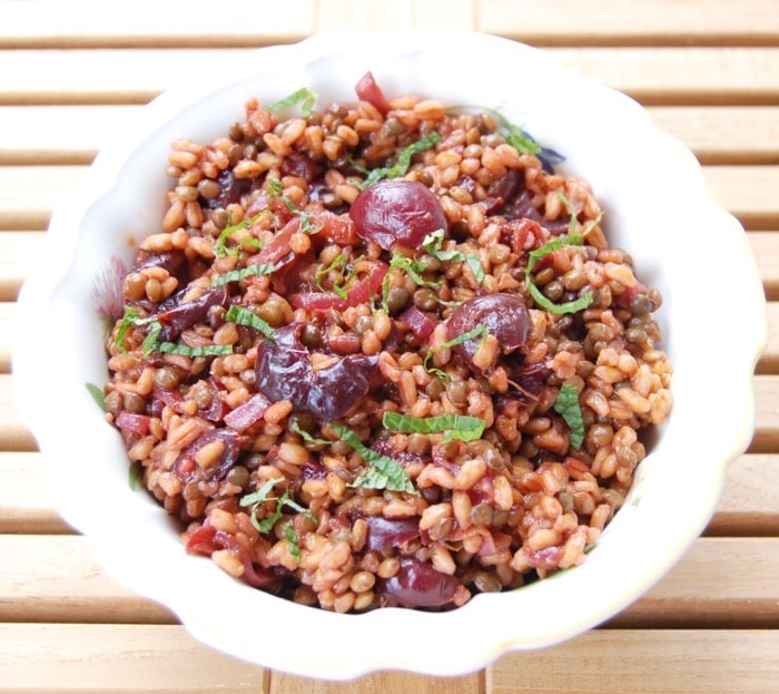 Birds eye close up image of plant-based roasted cherry and farro salad in a large white bowl, garnished with fresh herbs