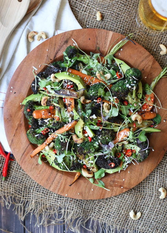 Birds eye image of vegan grilled broccoli, carrot and avocado salad with sesame dressing served in a large wooden bowl, garnished with additional sesame seeds and cashews.