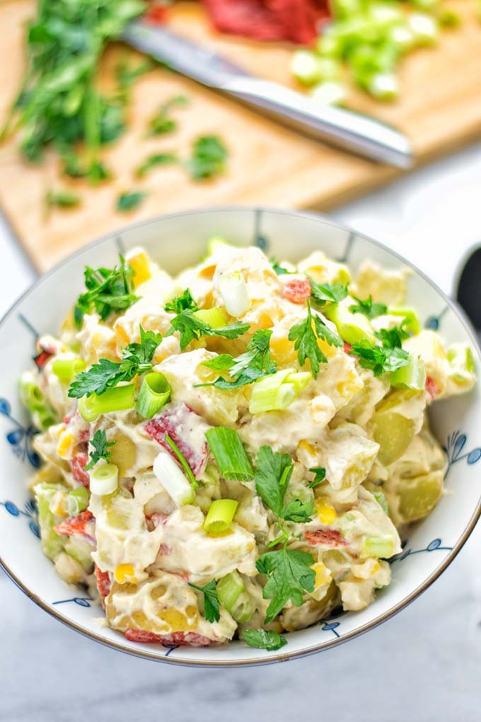 Close up of vegan hummus potato salad served in a white bowl with blue flower detailing, garnished with additional herbs and green onions