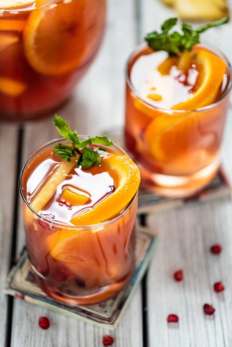 Close up image of kombucha sangria in short clear glasses on colourful square coasters, garnished with fresh mint and pomegranate seeds 