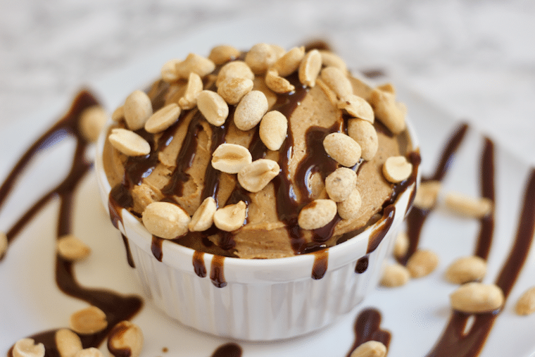 Close up of a mini vegan peanut butter pie served in a small white ramekin and garnished with chopped peanuts and a chocolate drizzle 