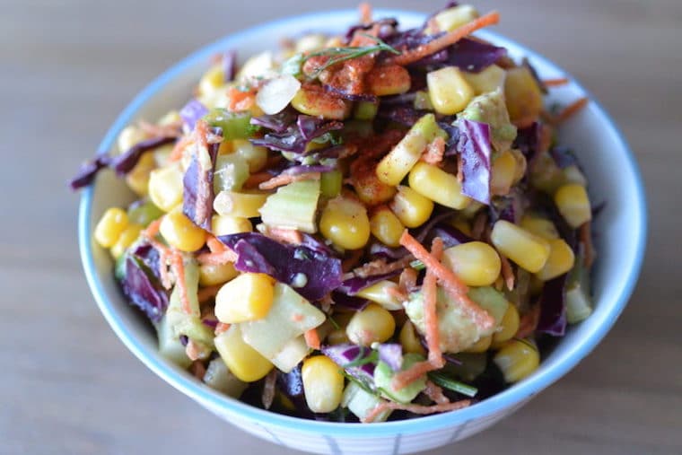 Close up image of rainbow slaw served in a blue and white bowl garnished with fresh herbs