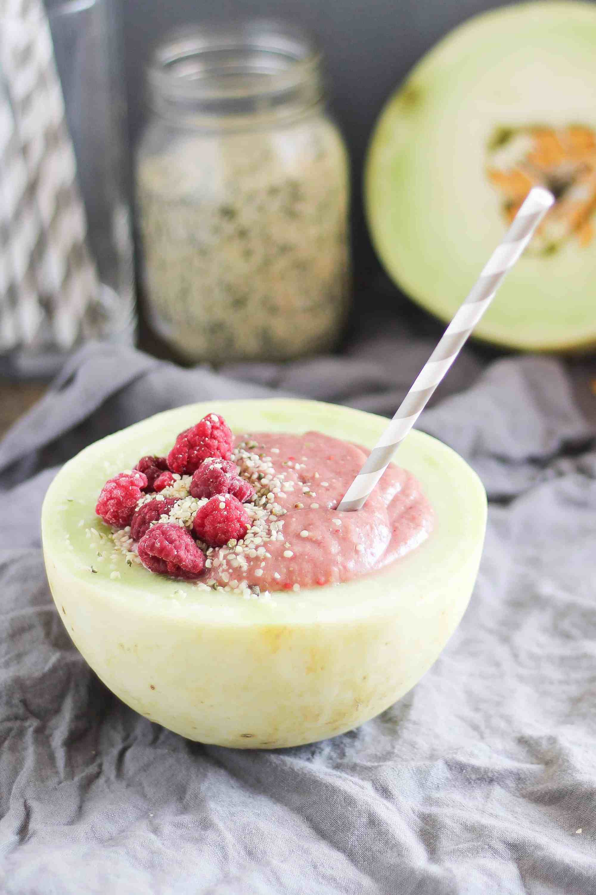 Smoothie served in a melon bowl topped with raspberries and hemp hearts. 