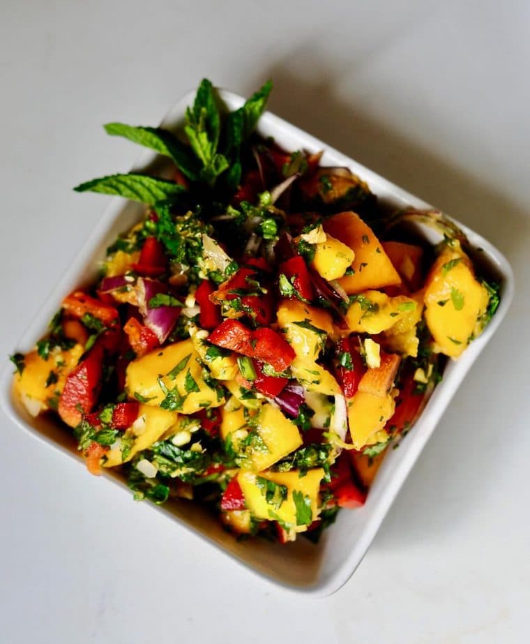 Close up of spicy ripe papaya salad served in a white square bowl garnished with additional fresh herbs