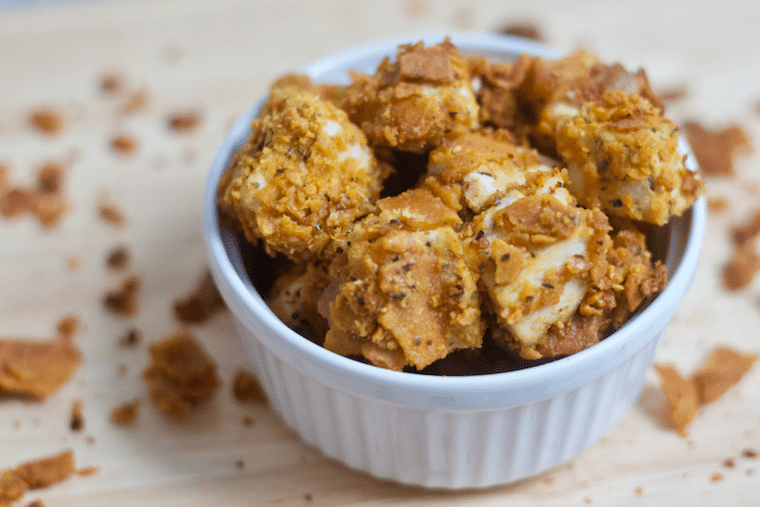 Close up shot of vegan cheesy tofu nuggets served in a white ramekin atop of a wooden surface