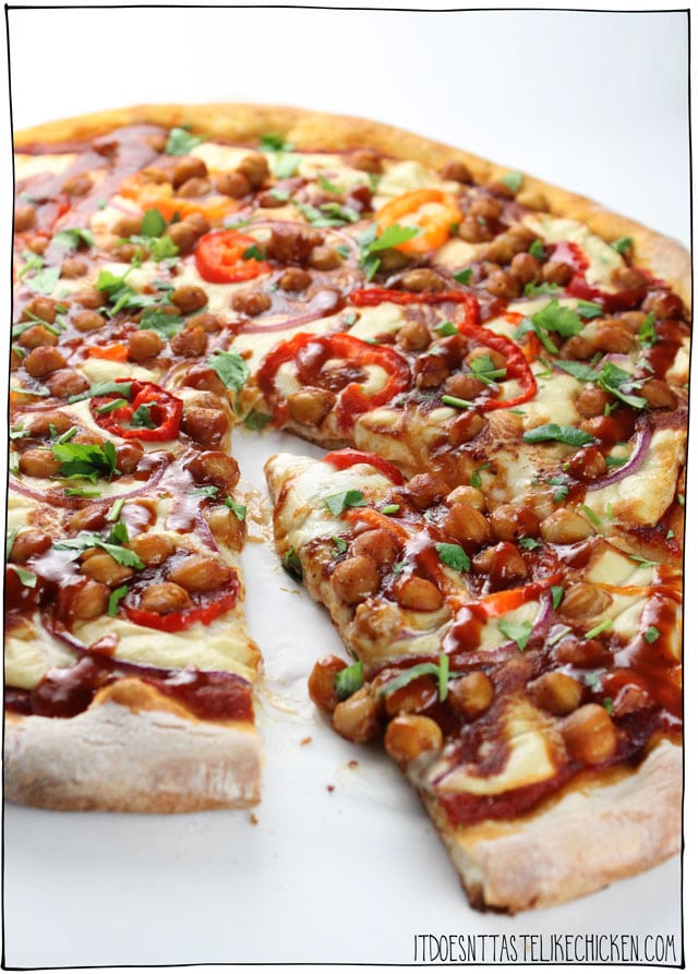 Close up of vegan barbecue chickpea pizza with one slice removed from the pizza, garnished with parsley and additional barbecue sauce 