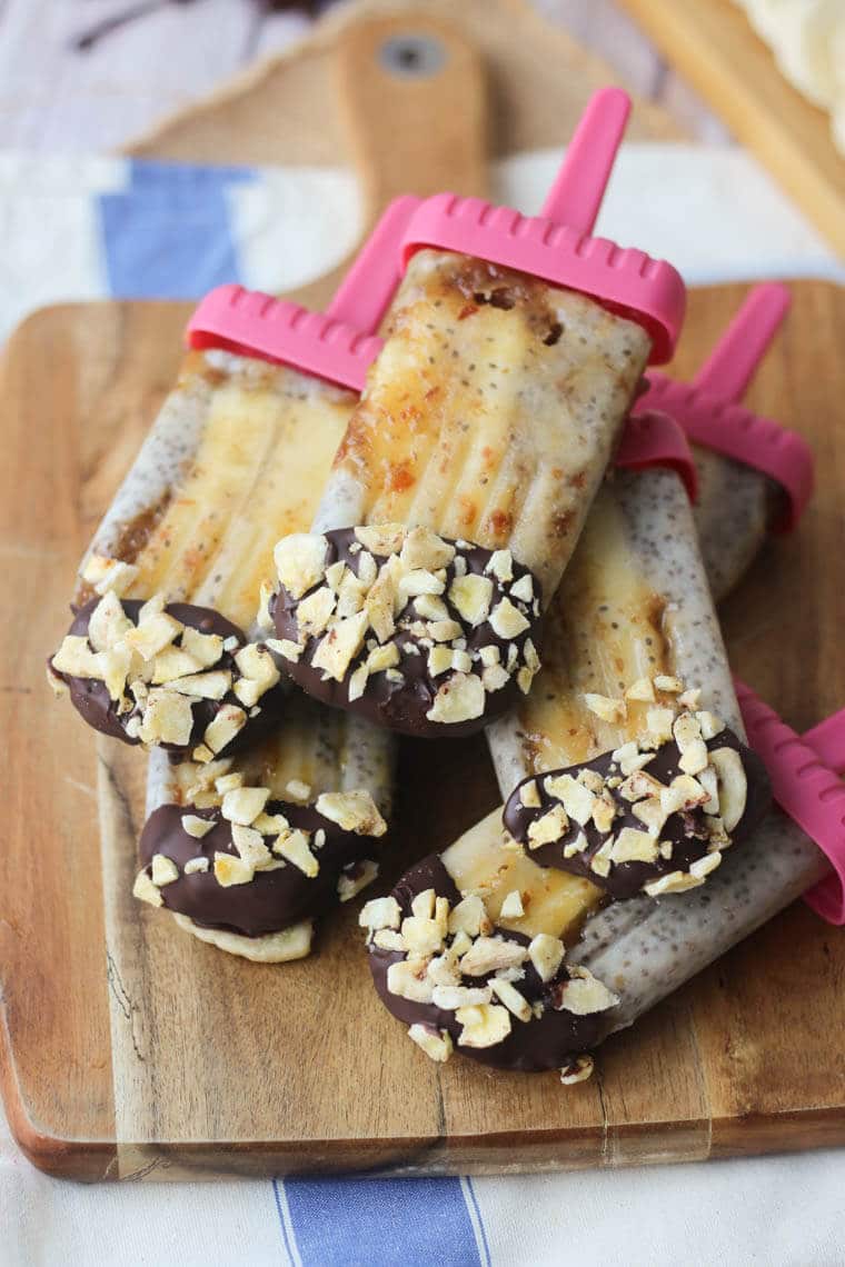 Close up image of vegan banoffee pie popsicles in pink popsicle holders stacked on top of one another on a wooden serving board