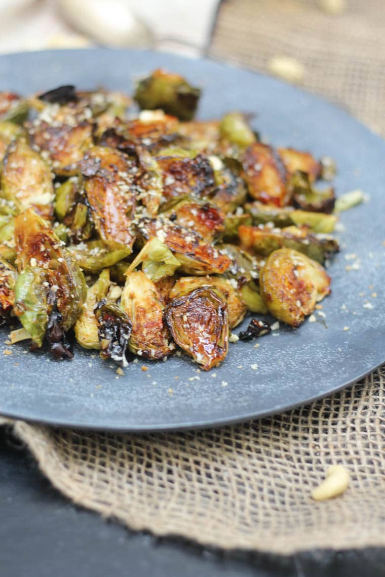 Close up of plant-based sweet-chilli roasted brussel sprouts garnished with a cashew topping served on a large blue dish 