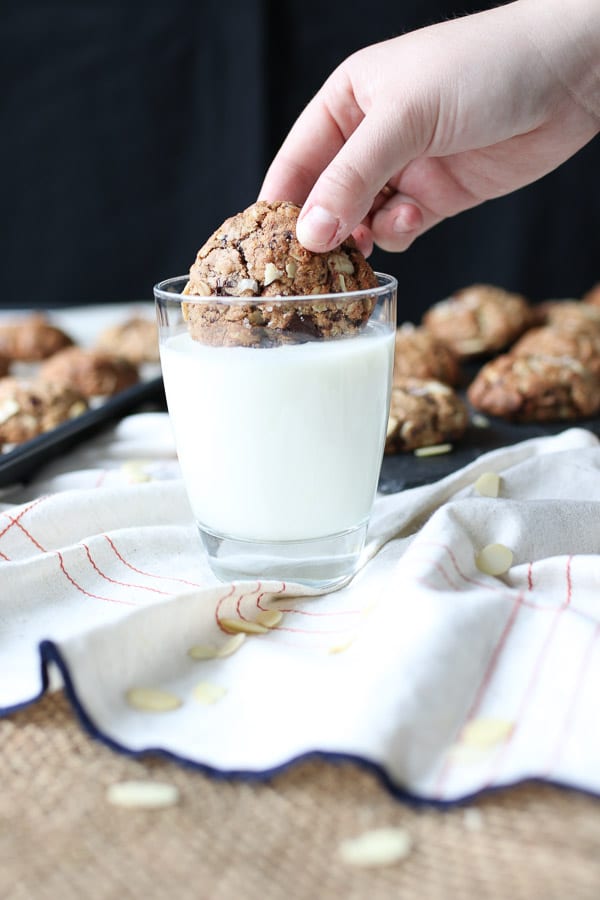 Hand dipping salted almond lactation cookie in a glass of milk.