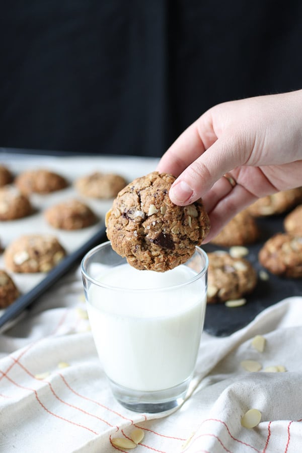 Hand holding a lactation cookie over a glass of milk.