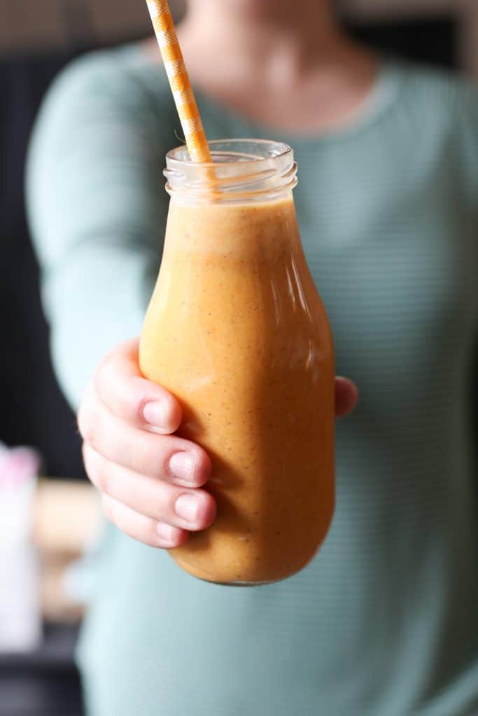 Person holding a Carrot Cake Lactation Smoothie with a yellow straw. 