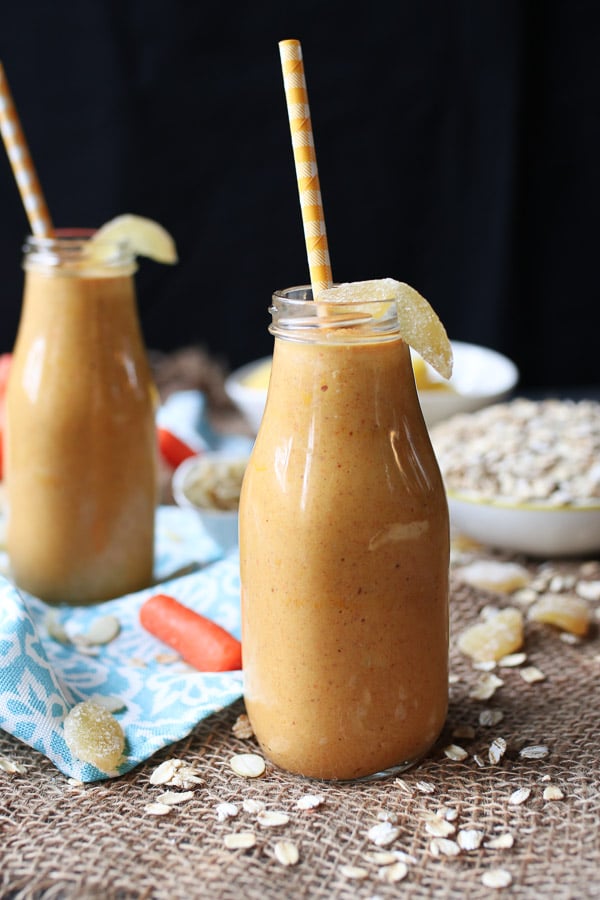 Vegan carrot cake lactation smoothie in a large glass with a straw and ginger candy on the rim. 