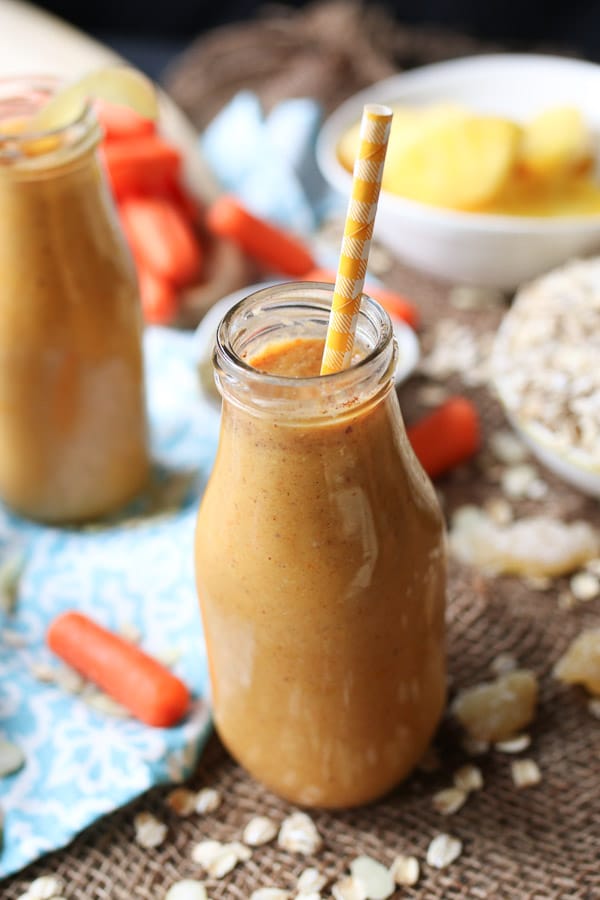Vegan carrot cake smoothie in a large glass with a straw and ginger candy on the rim.