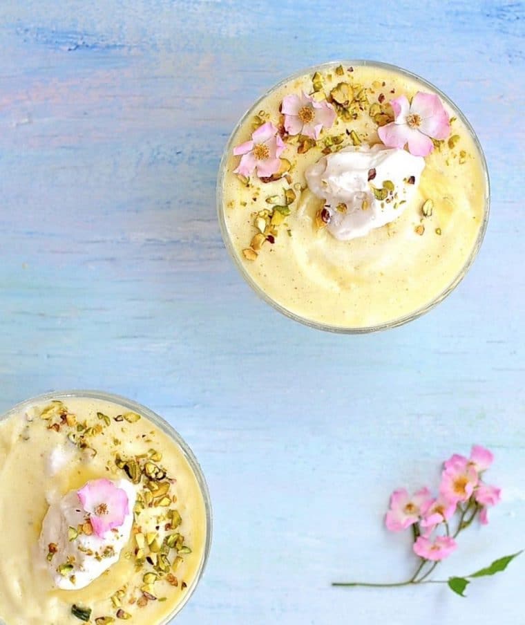 Birds eye view of plant-based lemon mousse served in bowls, garnished with pistachios, pink flowers, and vegan cream
