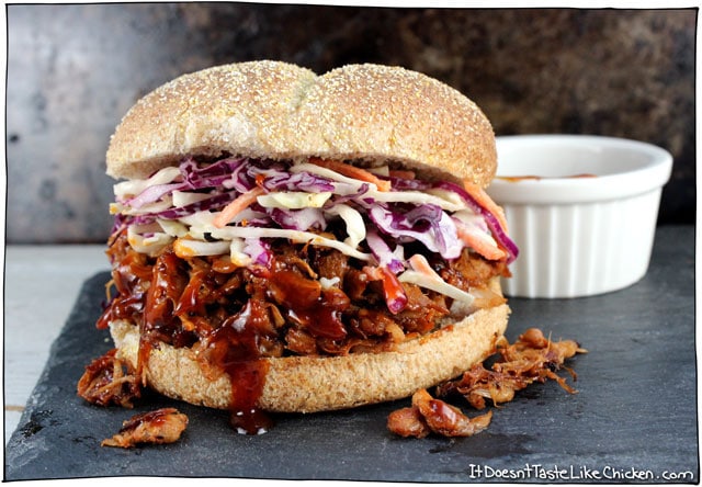 Close up of a plant-based six ingredient pulled jackfruit sandwich inside of a hamburger bun, featuring a small ramekin with extra sauce in the background 