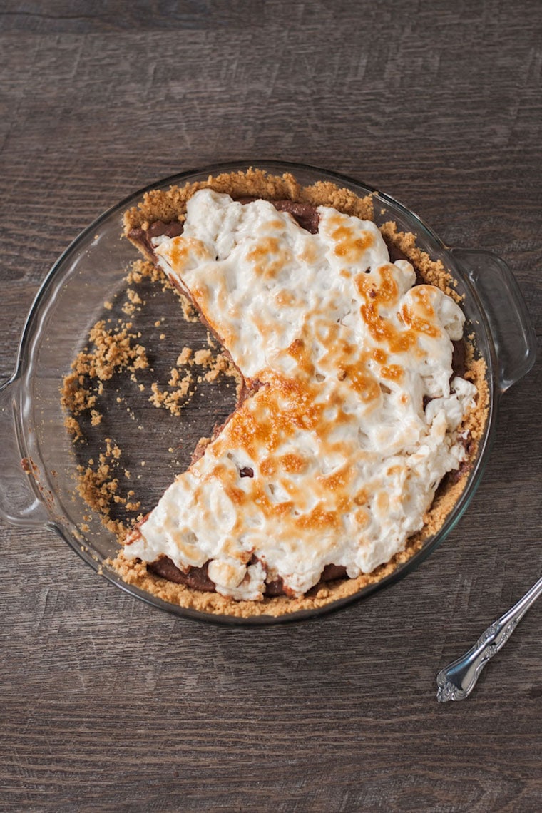 Birds eye view of plant-based s'mores pie with a slice cut out of it in a clear serving dish, garnished with additional graham cracker crumbs 