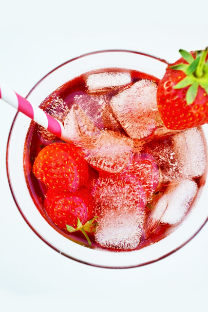 Birds eye image of strawberry sip summer cocktail served in a clear glass with a pink and white straw, garnished with fresh strawberries