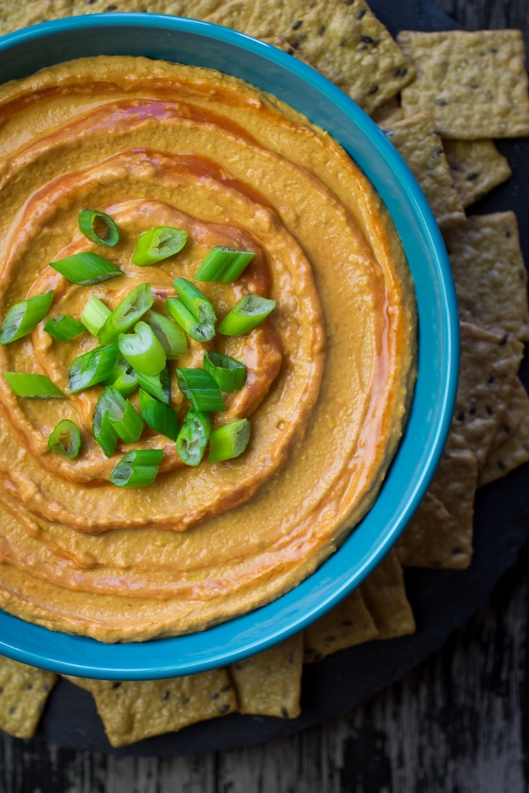 Buffalo white bean hummus topped with green onions next to crackers. 