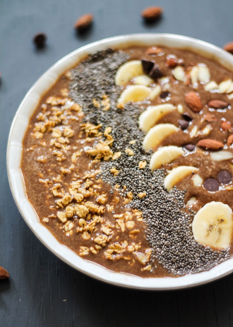 close up of mocha banana protein smoothie bowl topped with nuts, seeds, and fruit