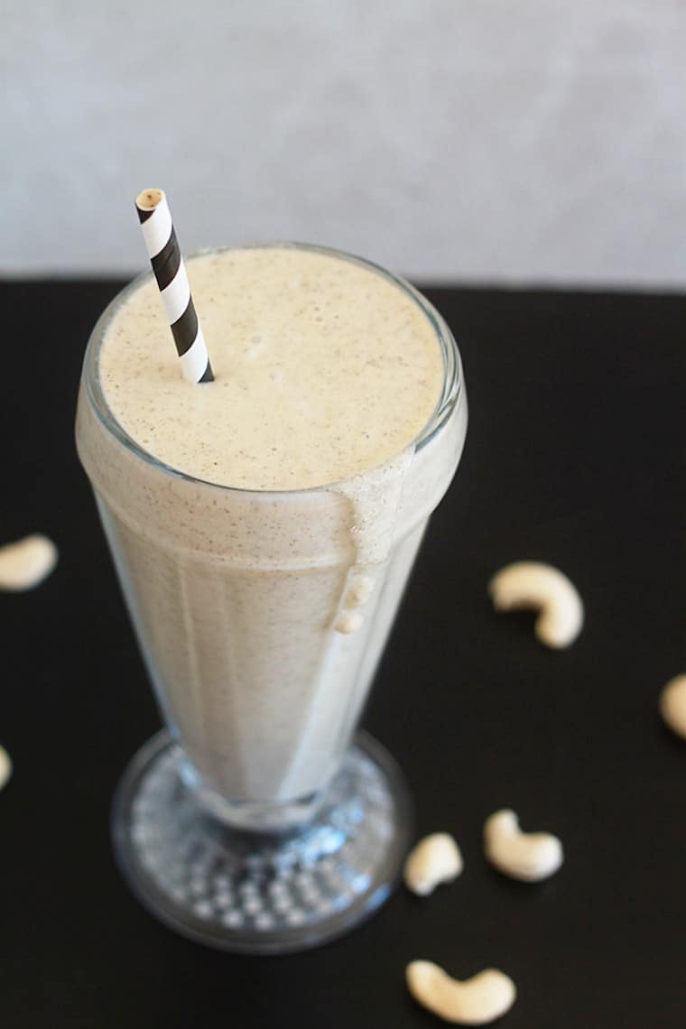 close up vanilla cashew shake in a tall clear glass with a black and white straw