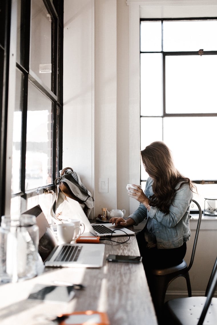 Woman working on her laptop holding a cup. 