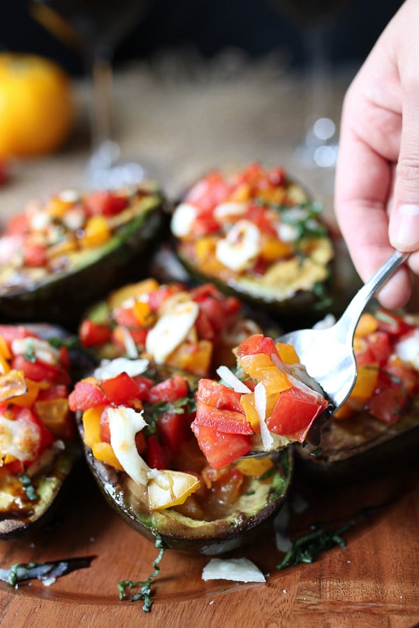 Hand holding a spoon digging into grilled avocado bruschetta. 