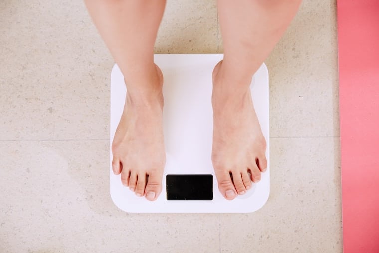 Woman standing on a scale referring to the question "Can you diet while pregnant?".