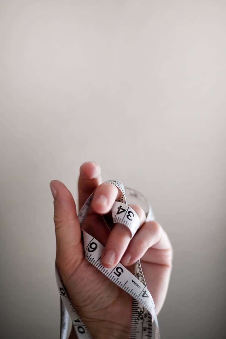 A hand holding a measuring tape referring to the question "Can you diet while pregnant?".