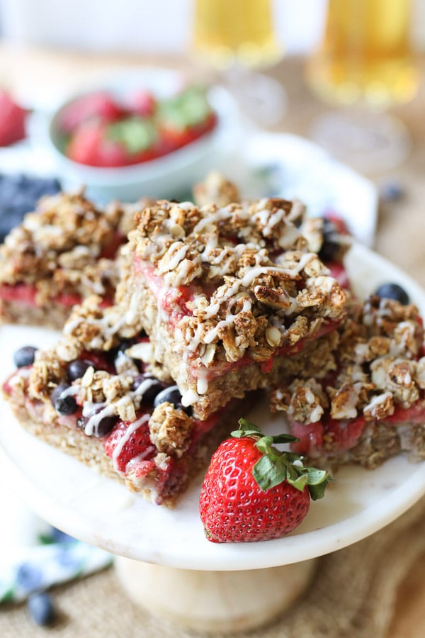 oat bars with berries stacked on a white plate with a strawberry on the side.