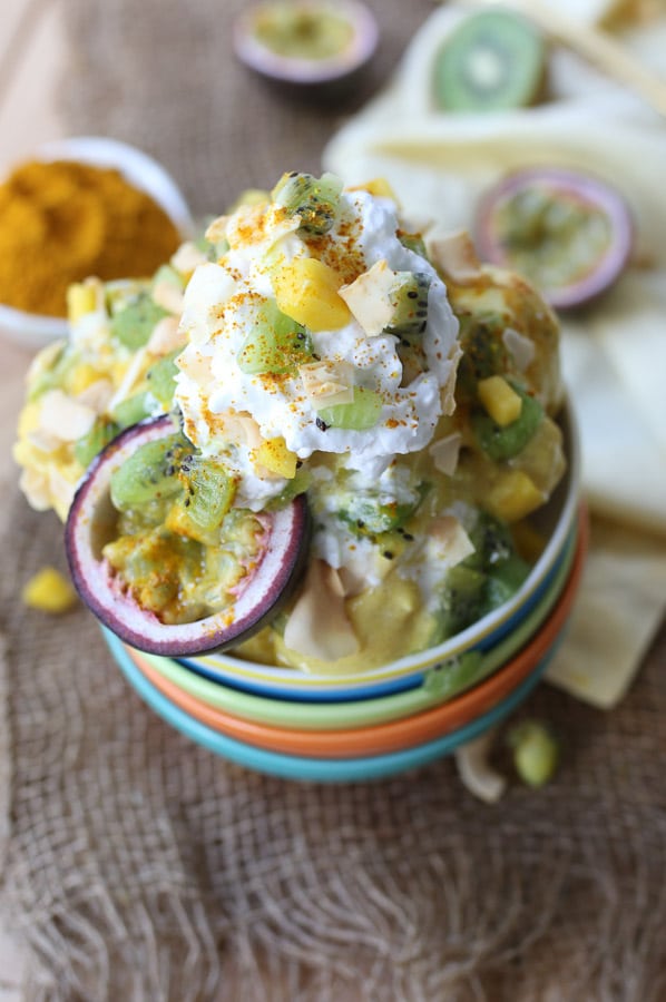 close up of vegan turmeric golden milk nice cream sundae in a colourful bowl topped with fresh fruit