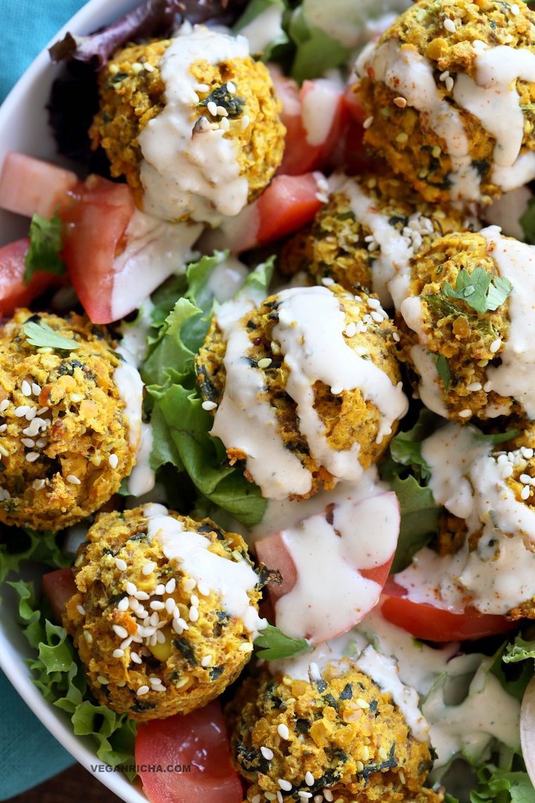 close up of turmeric lentil fritters in a salad bowl topped with tahini